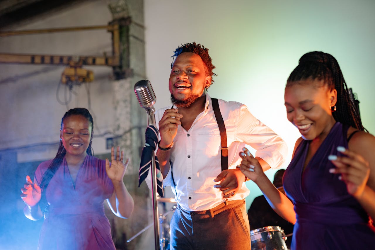 A lively group of adults singing and dancing with a vintage microphone indoors.